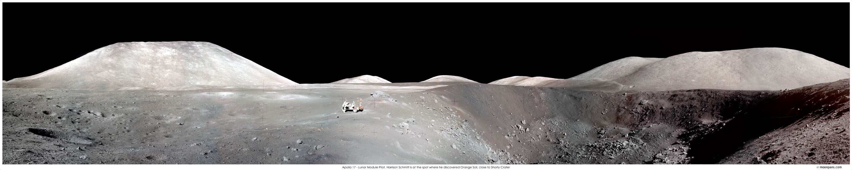 Das breite Panorama zeigt die Mondoberfläche. Am Horizont ragen Berge hoch, dahinter ist die Schwärze des Weltraums. In der Bildmitte steht das Mondauto mit einem Astronauten, rechts daneben ist der Krater Shorty.