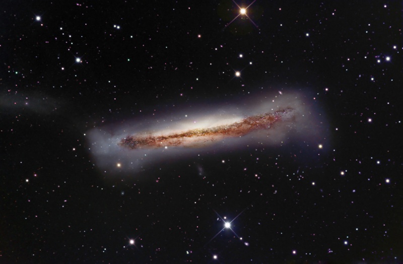 Die Galaxie im Bild ist von der Seite sichtbar, in der Mitte ist ein starkes Staubband, außen herum wirkt sie sehr milchig-verschwommen