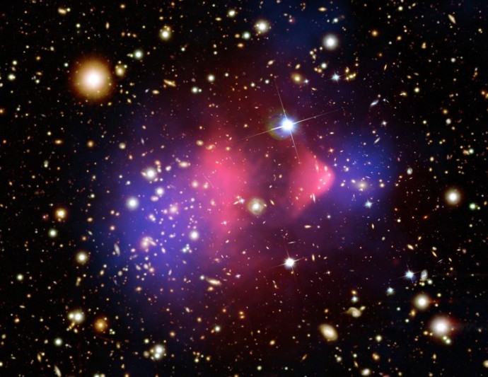 Im Bild sind zahlreiche Galaxien wie Sterne verteilt. im Hintergrund leuchten magenta- und blaufarbige Wolken.