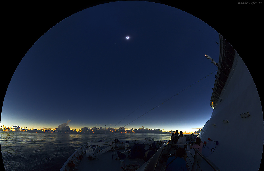 An einem dunkelblauen Himmel leuchtet die Korona der Sonne bei einer totalen Sonnenfinsternis. Am Horizont ist der Himmel hell.