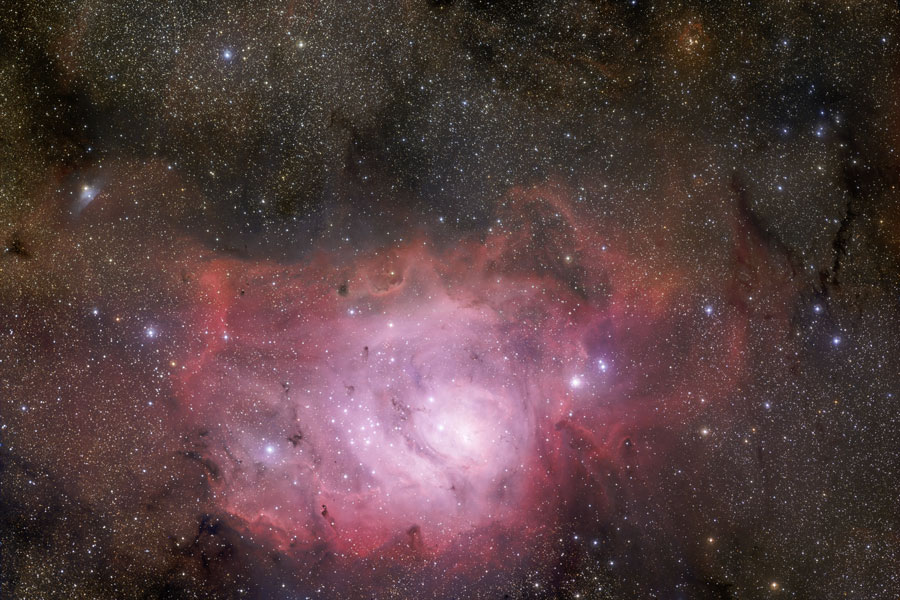 In einem sternenübersäten Bild leuchtet unten ein roter Nebel wie eine Höhle mit einem hellen Inneren.