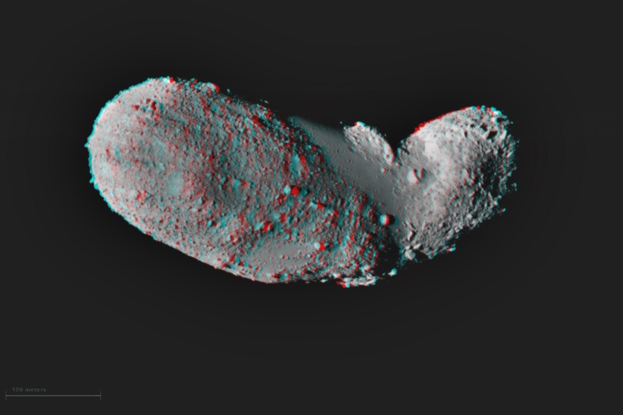 Das rot-blaue Bild zeigt den Asteroiden Itokawa. Er ist von Geröll übersät und hat eine längliche, leicht gewinkelte Form.