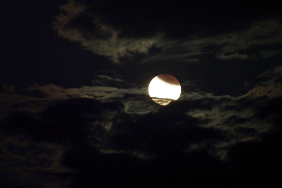 Mitten im Bild leuchtet der Vollmond, unten wird er teilweise von einigen Wolken verdeckt, oben vom Schatten der Erde.