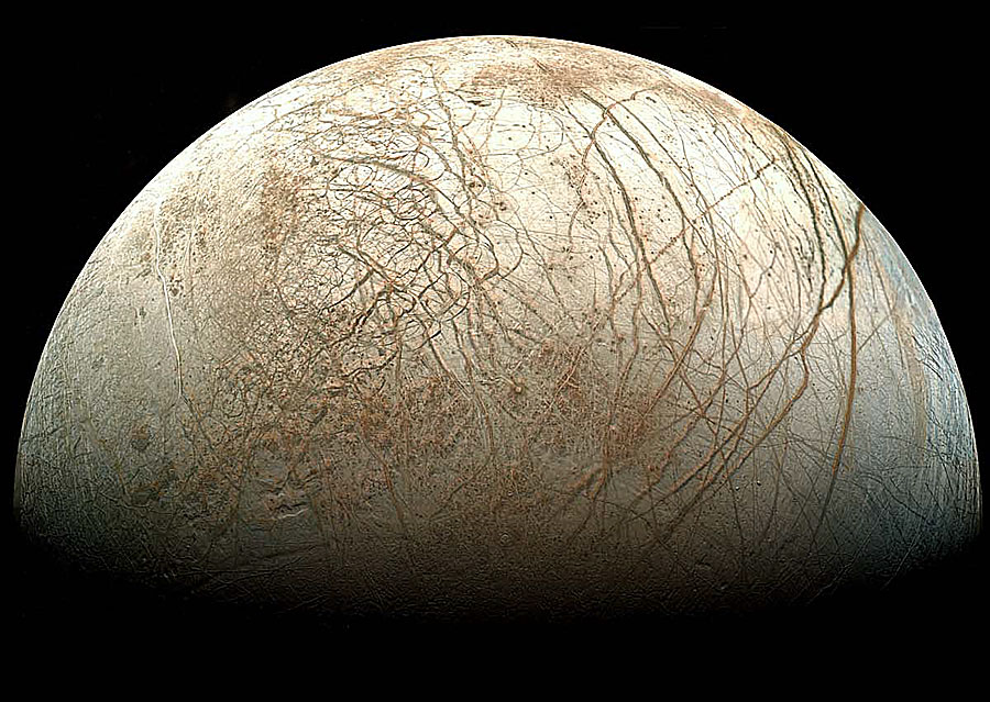 Etwa die Hälfte des Jupitermondes Europa ist beleuchtet und ragt nach oben ins Bild. Der beige-weiße Mond ist von vielen rötlichen Rissen überzogen.