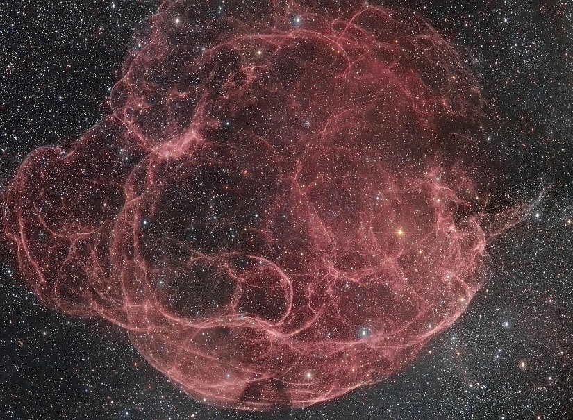 Wie ein Knäul aus roten Fäden schlingen sich die Wirbel in diesem Supernovaüberrest in einer Umgebung, die dicht von Sternen gesprenkelt ist.