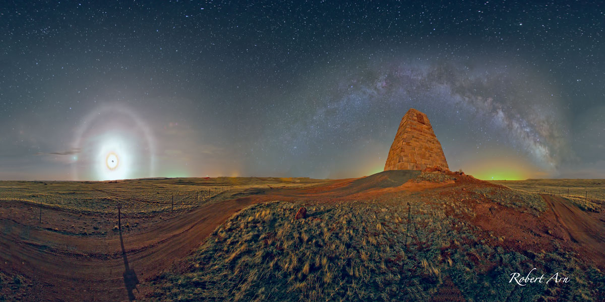 Links gdht der Mond unter, mitsamt Mondhof und Mondkorona. Rechts wölbt sich die Milchstraße über dem Ames-Monument in Wyoming.