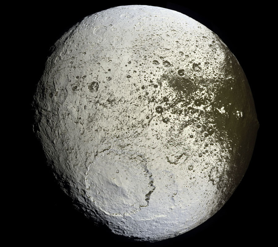 Der Saturnmond Iapetus ist hell wie Eis, er füllt fast das ganze Bild. Unten ist ein riesiger Krater mit Zentralberg, rechts ist er dunkel befleckt oder beschmutzt.