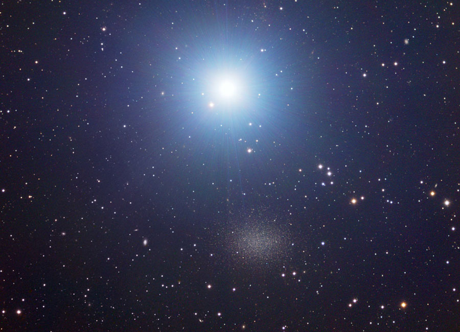 Unter einem sehr hellen Stern mit blauem Hof befindet sich eine kleine, kaum erkennbare Galaxie, deren Aussehen an einen Kugelsternhaufen erinnert.