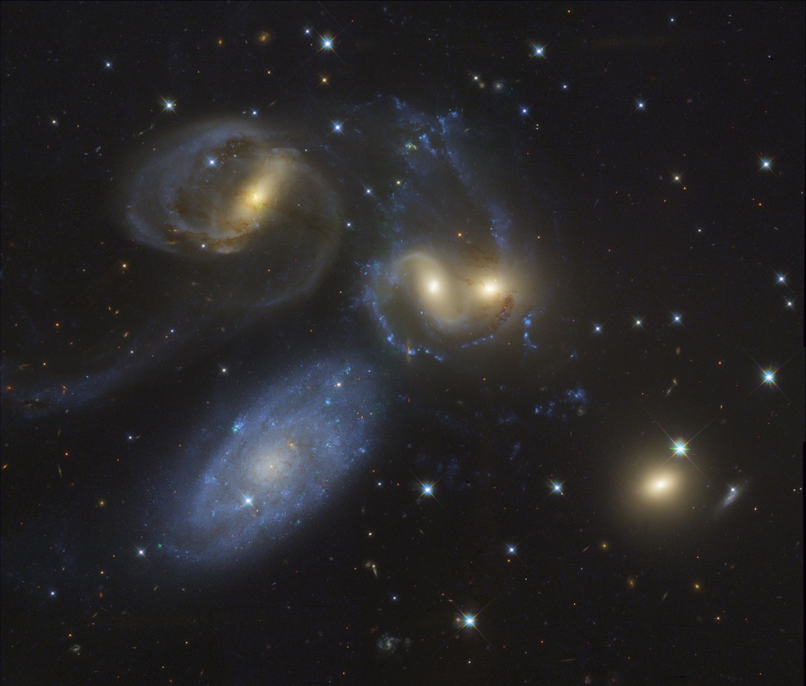 Im Bild sind fünf Galaxien zu sehen, vier davon leuchten gelblich und sind gleich weit von uns entfernt. Links unten ist eine bläuliche Spiralgalaxie ohne Verzerrung, die viel näher ist als die anderen Galaxien.