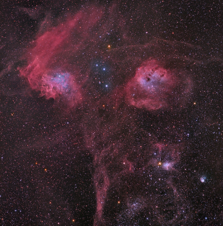 Hinter kleinen, dicht verteilten Sternen sind prachtvolle rot leuchtende Nebel und Sternhaufen verteilt.