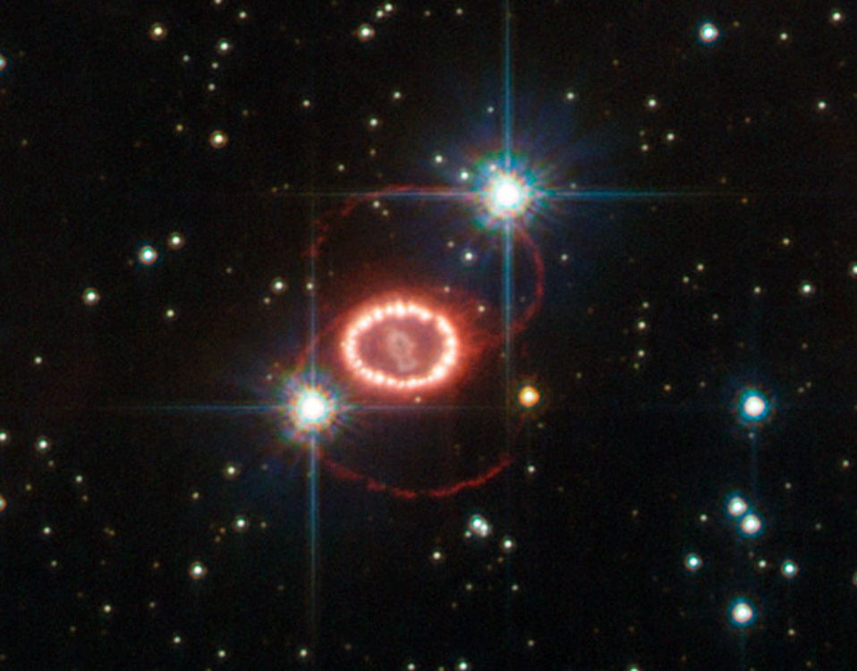 Mitten im Bild leuchtet ein Ring aus lellen Lichtern. Von diesem gehen nach oben und unten dunkelrote Ringe aus, die eine 8 bilden und nur schwach leuchten. Darum verteilt leuchten Sterne in unserer Milchstraße.