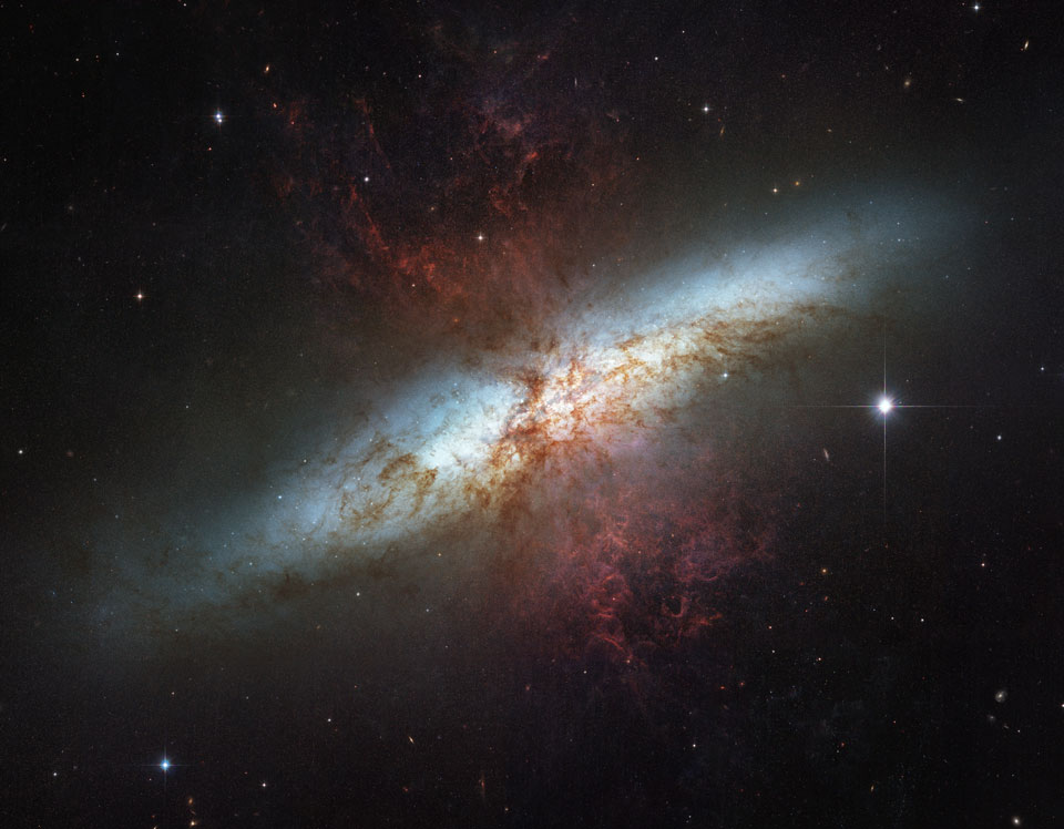 Die Galaxie im Bild ist unregelmäßig geformt, in der Mitte sind unregelmäßig geformte Staubfilamente über die Galaxie gelegt.