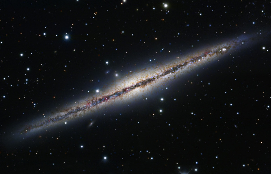 Diagonal im Bild verläuft eine Galaxie, die wir von der Kante sehen. Quer durch die Mitte verlaufen dunkle Staubwolken.