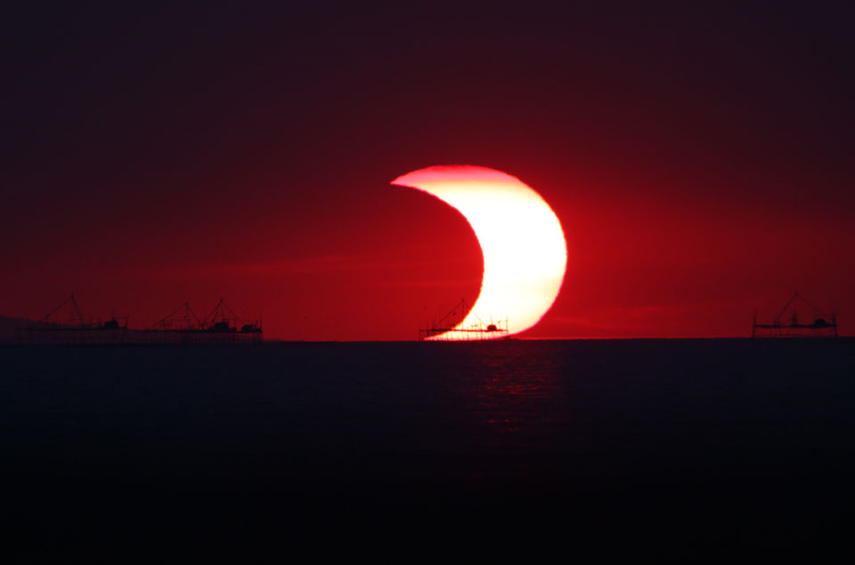 Sonnenfinsternis über der Bucht von Manila auf den Philippinen. Die Sonne ist zum Teil vom Mond bedeckt, über dem Kai leuchtet eine breite Sichel.