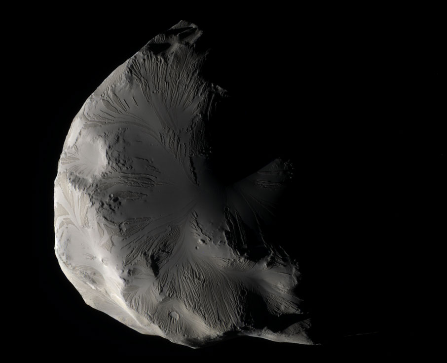 Der Mond im Bild wirkt schwarz-weiß, doch es ist ein Farbbild. Der Mond Helene hat eine eigenartige, geriffelte, teils glatte Oberfläche mit wenigen Kratern.
