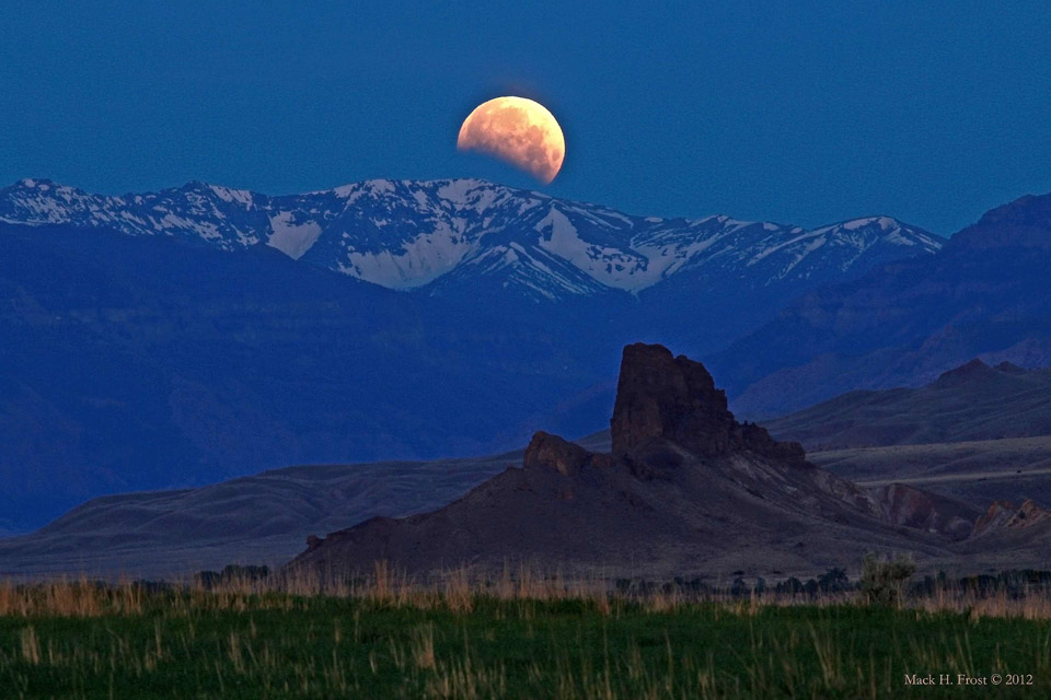 Hinter einem teils schneebedeckten Gebirge geht der Mond unter, der teilweise vom Erdschatten verfinstert ist. Im Vordergrund ist ein ungewöhnlich geformter Fels, der Horse's Head beim Shoshone River.