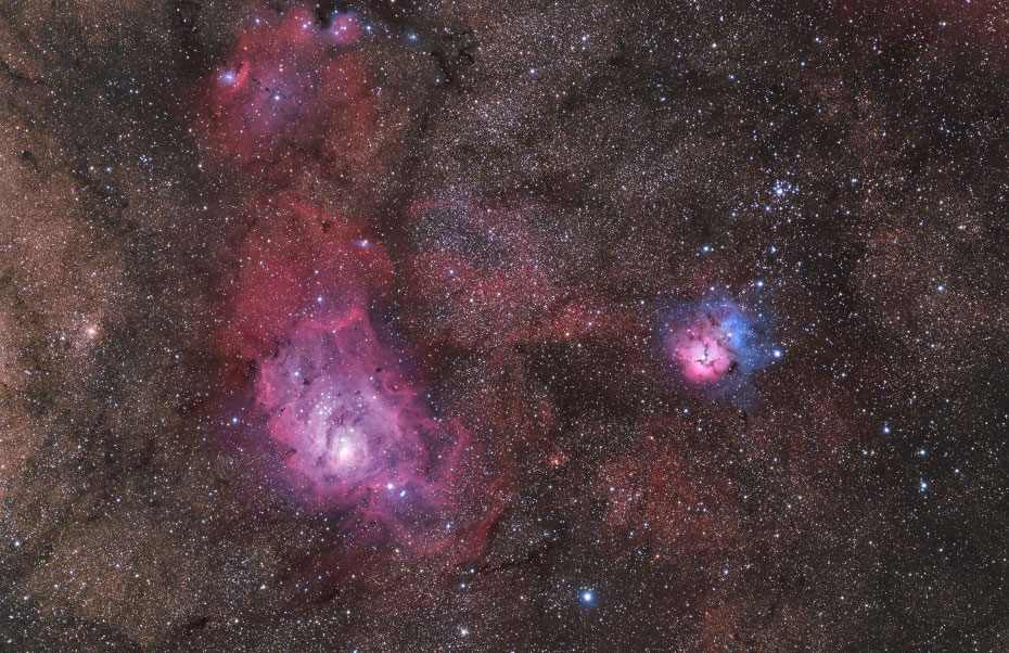 In einem sterngefüllten Sichtfeld mit dunklen Staubwolken leuchtet links in Magenta der Lagunennebel, rechts daneben der kleiner blau-rote Trifidnebel mit den markanten Staubranken.