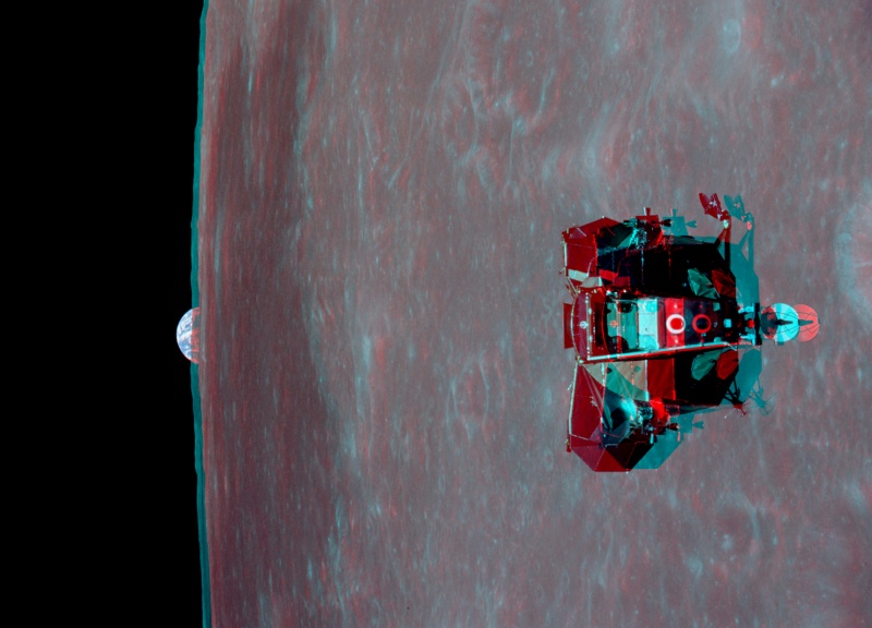 Das Bild in Cyan und Rot ist eine Anaglyphe. Rechts ist fast bildfüllend der Mond, links ragt ein Stückchen von der Erde über den Mondrand. Rechts schwebt das Mondlandemodul Adler von Apollo 11 vor dem Mond.