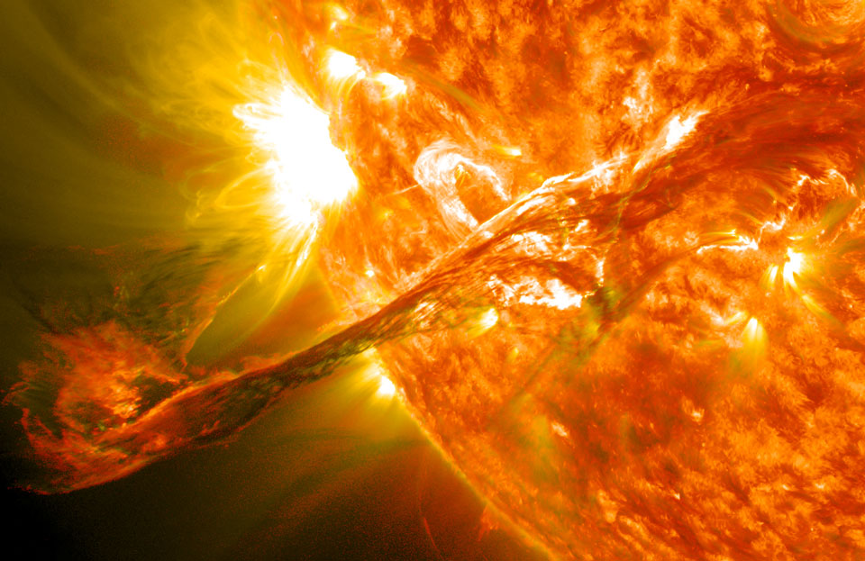 Rechts ragt ein Teil der Sonne ins Bild. Am linken Sonnenrand leuchtet eine helle Aktive Region, und quer über das ganze Bild verläuft eine Protuberanz, die links weit ins All hinausreicht.