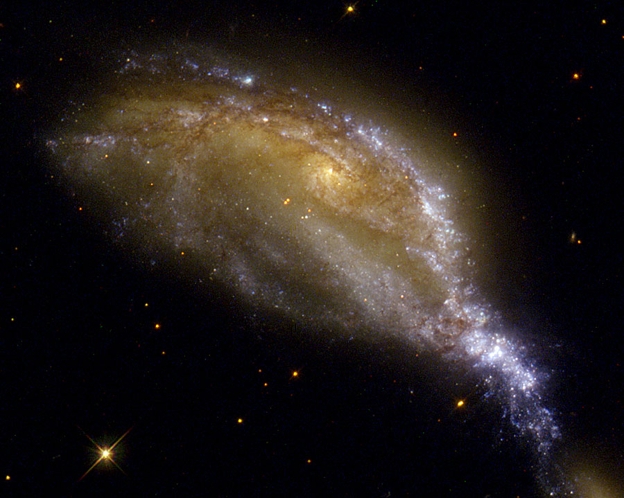 Die Spiralgalaxie mitten im Bild hat mehrere nahe Begegnungen und Kollisionen hinter sich und wirkt stark verzerrt.