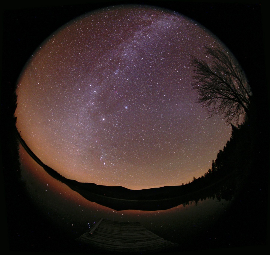 Das Bild zeigt den ganzen Himmel. Zu den auffälligen Erscheinungen zählt die Milchstraße, das Zodiakallicht mit Gegenschein und Nachthimmellicht. Der Jäger Orion mit seinen hellen Gürtelsternen spiegelt sich im Wasser des Sees.