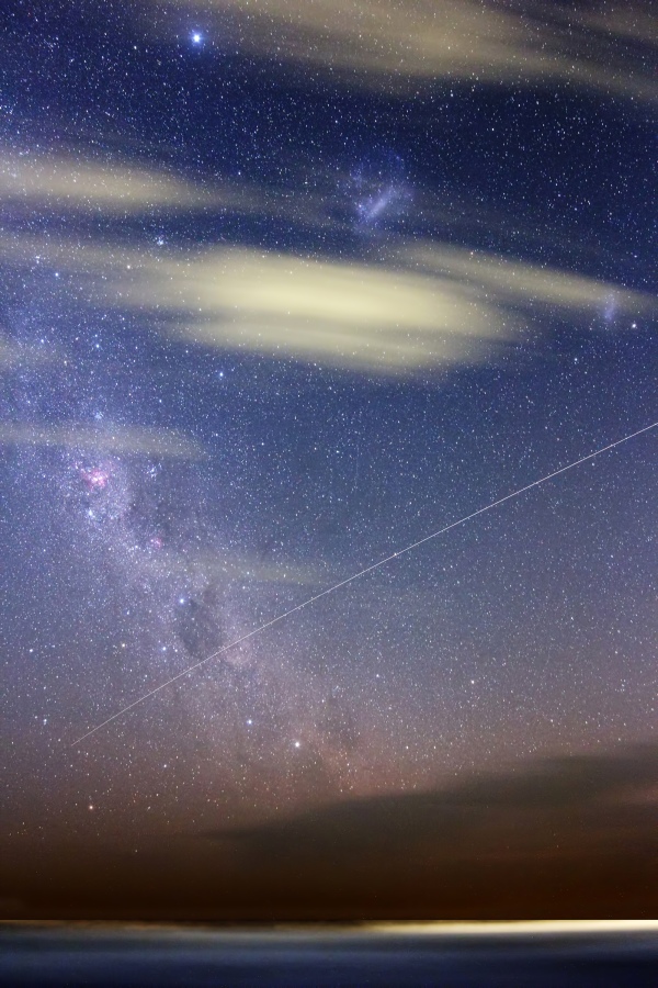 Über dem wolkenverhangenen Meer bei Buenos Aires in Argentinien ist der prächtige Südhimmel zu sehen. Links steigt die Milchstraße mit dem Kohlensacknebel auf, oben leuchten die Große und die Kleine Magellansche Wolke, und die Internationale Raumstation ISS zieht diagonal eine Leuchtspur durchs Bild.