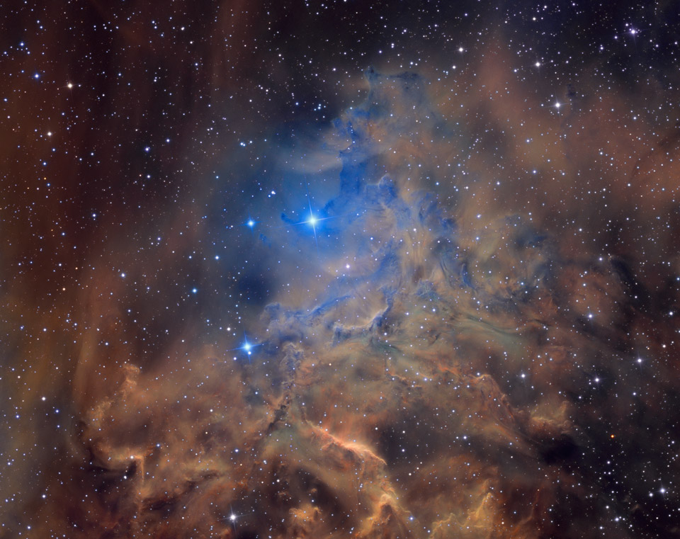 Im Bild sind braune, teils beleuchtete Nebel verteilt, die in der Mitte in einen blauen Nebel übergehen, der zwischen den braunen Nebelwolken hindurchschimmert. Die im Bild dünn verteilten Sterne sind eher blass.