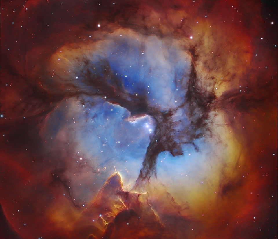 Im Bild leuchtet der sonst rot abgebildete Trifidnebel blau, die dreiteilenden Dunkelwolken sind viel ausladender als sonst. Das blaue Innere des Nebels ist von einem orangefarbenen Rand umgeben, der in Dunkelrot und Braun übergeht. In der Mitte leuchten einige helle Sterne.