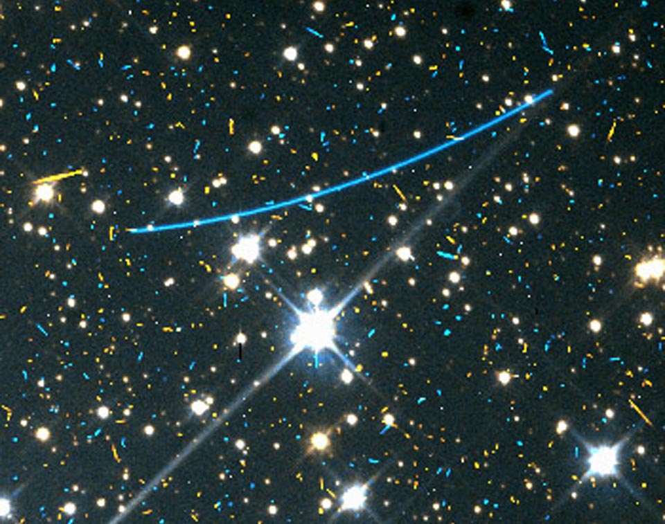 Vor einem stark vergrößerten Sternenfeld verläuft ein blauer Bogen. Es ist ein Asteroid, der auf einem Archivbild des Weltraumteleskops Hubble gefunden wurde.