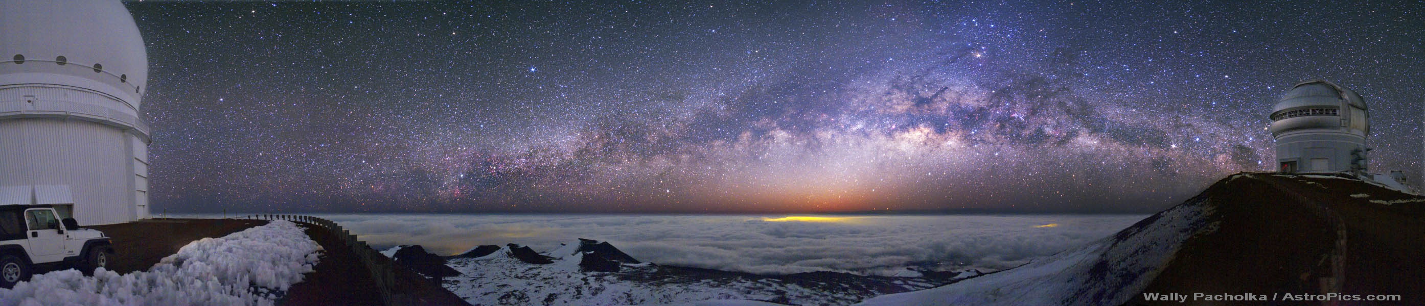 Das breite Panorama zeigt die Milchstraße, die sich über dem Horizont zwischen zwei Teleskopkuppeln ausbreitet. Links steht das Canada-France-Hawaii-Teleskop CFHT, rechts das Observatorium Gemini Nord.