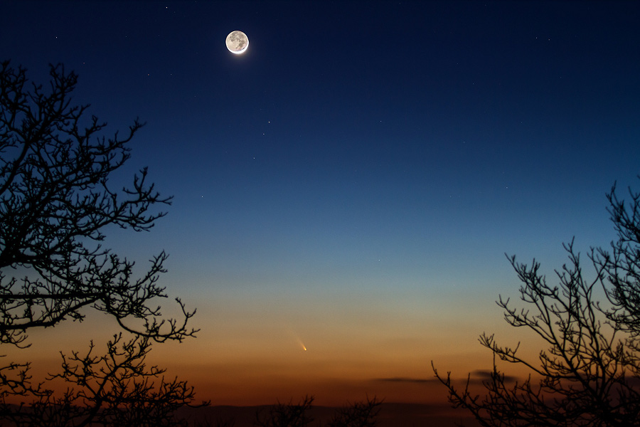 Der klare Himmel zeigt unten ein intensives Abendrot und ist oben tiefblau. Tief im Westen steht der kommt PanSTARRS, oben leuchtet der Sichelmond, dessen Nachtseite ebenfalls hell im Erdlicht strahlt.