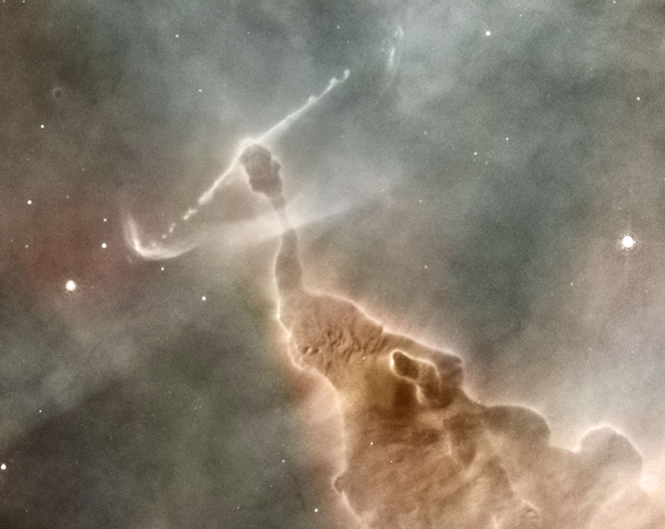 Das Bild zeigt eine Staubsäule im Carinanebel. Von links unten ragt ein seltsames Monster ins Bild. Aus seinem Kopf strömen links und rechts helle Strahlen.