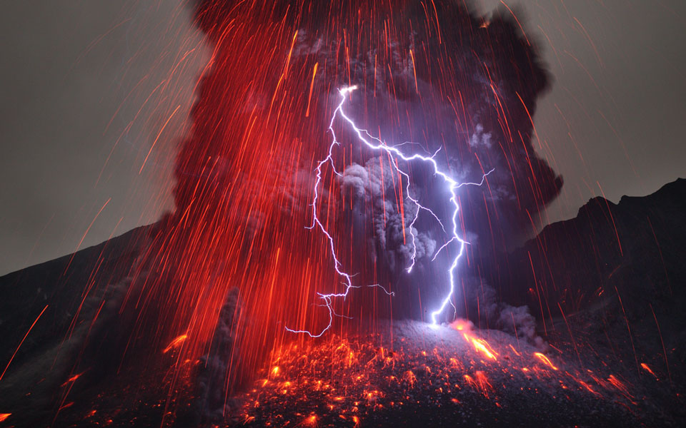 Aus einer vulkanischen Aschewolke mit rot glühender Lava schlagen Blitze.
