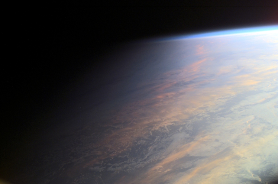 Die Sonne scheint von rechts auf den Planeten Erde, der nach links hin allmählich in die dunkle Nachtseite des Planeten Erde verläuft. Oben ist ein blauer Rand, es ist die Troposphäre.