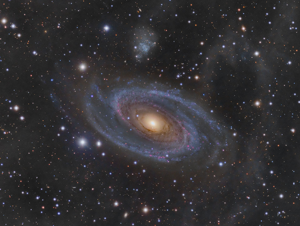 Mitten im Bild dreht sich die Spiralgalaxie M81 im Sternbild Große Bärin. Sie besitzt zwei ausgeprägte Spiralarme, ist aber keine Balkenspiralgalaxie. Ihr gelber Kern bildet einen starken Kontrast zu den blauen Spiralarmen.