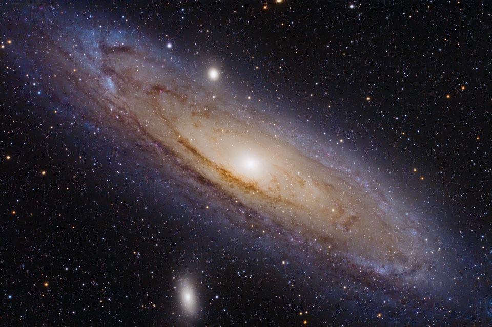 Die Andromedagalaxie M31 füllt das Bild. Auch ihre Begleitgalaxien M32 und M110 sind abgebildet. Ihre Scheibe wirkt leicht gekrümmt, sie ist von dunklen Staubranken durchzogen. Das Innere leuchtet eher gelblich, das Äußere bläulich.