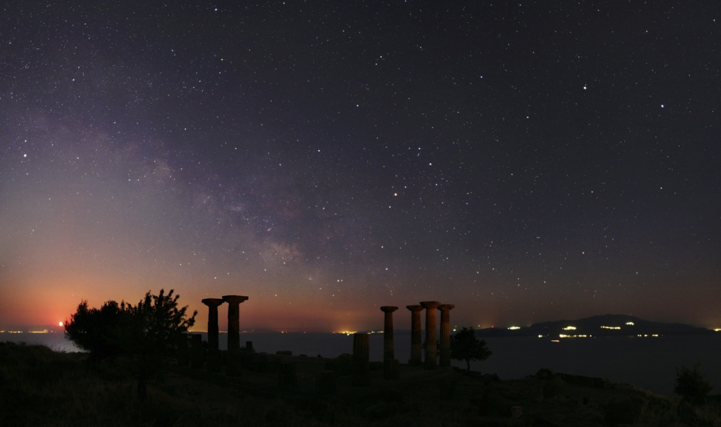 Hinter dem Athena-Tempel im türkischen Assos leuchtet ein Nachthimmel mit Milchstraße und dem Planeten Saturn. Das rötliche Licht links hinten am Horizont stammt vom Mond.