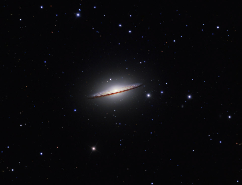 Zwischen lose verteilten Sternen schwebt die Galaxie M104. Sie liegt schräg im Raum und zeigt fast mit der Kante auf uns. Ihr Aussehen erinnert an einen Sombrero.