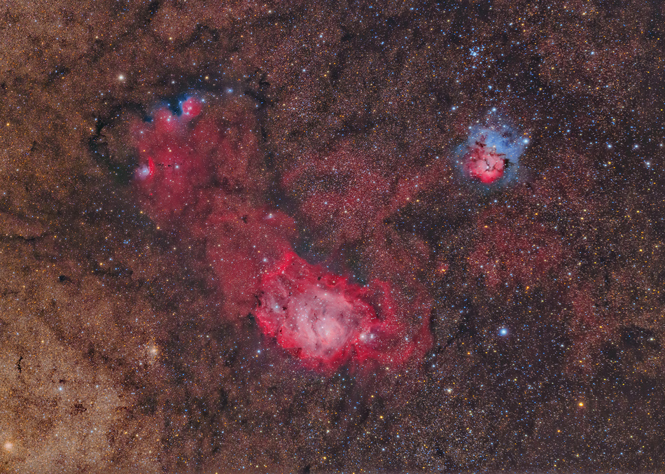 Links leuchten die roten Nebel M8, auch Lagunennebel genannt, und NGC 6559. Rechts oben ist der Trifidnebel, der als M20 katalogisiert ist. Trifid ist der kleinste der drei, aber der farblich kontrastreichste. Im Hintergrund leuchtet ein Teppich voller Sterne.