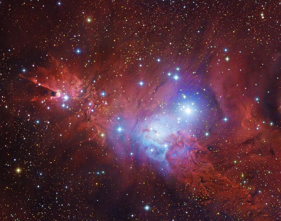Mitten in rot leuchtenden Nebelwolken strahlt ein blauer Reflexionsnebel um junge, helle Sterne. Von links ragt der Kegelnebel ins Bild. Der rote Nebel rechts unten erinnert an ein Fuchsfell.