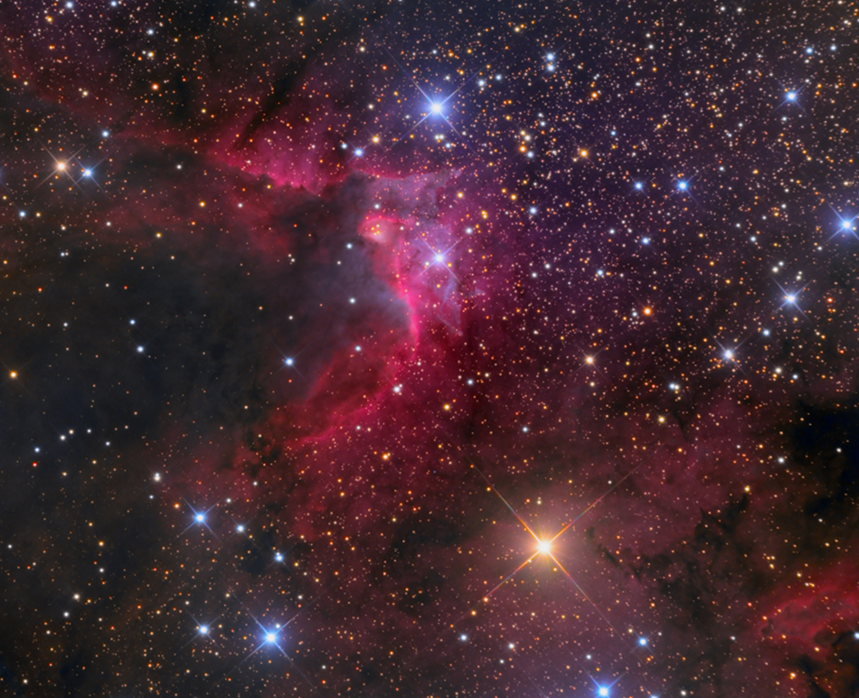 Eine Dunkelwolke ragt von links ins Bild, sie wird in der Mitte von den Sternen einer OB3-Sternassoziation im Sternbild Kepheus ionisiert und leuchtet rötlich.