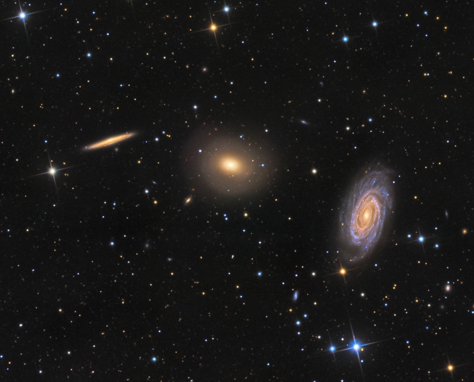 Drei Galaxien bilden einen interessanten Kontrast: Links ist eine Spiralgalaxie von der Seite zu sehen, rechts eine Spiralgalaxie von schräg oben, in der Mitte befindet sich eine elliptische Galaxie.