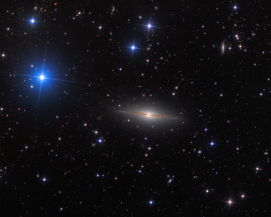 Die Galaxie im Bild erinnert entfernt an den Sombreronebel M104. Sie hat eine große diffuse Wölbung, die von einer Scheibe und Staubbahnen durchschnitten wird.