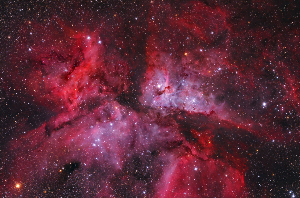 Im Bild leuchtet ein roter Emissionsnebel im Sternbild Schiffskiel, der von Dunkelwolken geteilt ist.