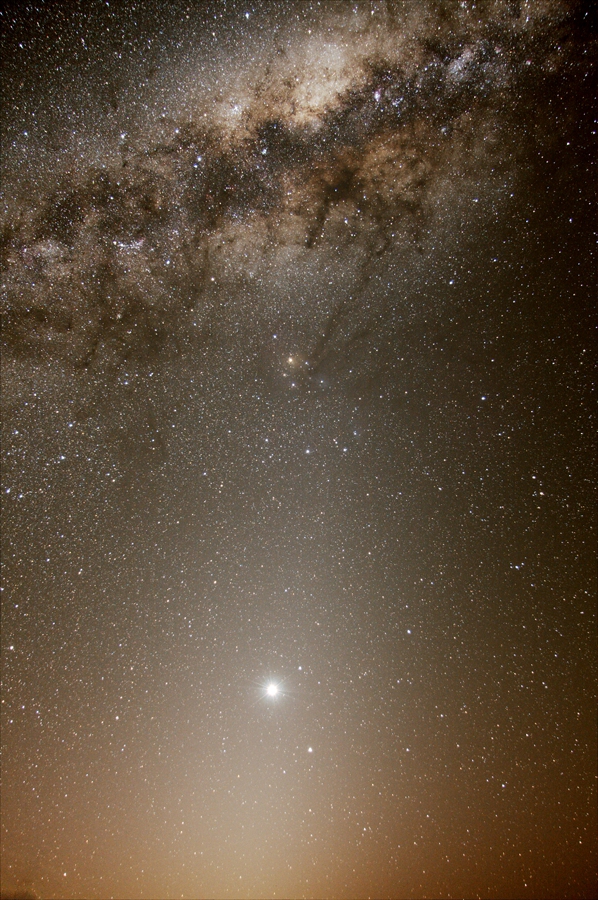 Oben wölbt sich das Zentrum unserer Milchstraße mit dunklen Staubwolken, darunter leuchtet der helle Planet Venus, und vom Horizont steigt Zodiakallicht pyramidenförmig auf.