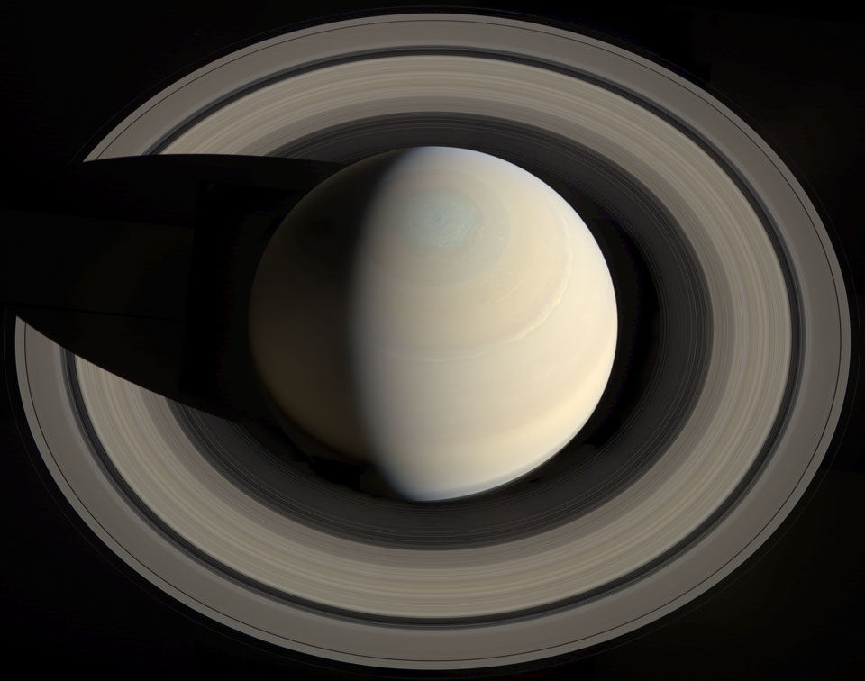 Saturn ist schräg von oben zu sehen. Der Planet wirft einen Schatten auf die Ringe. Das Wirbelsturm-Sechseck, das den Nordpol umgibt, ist ganz von der Sonne beleuchtet.