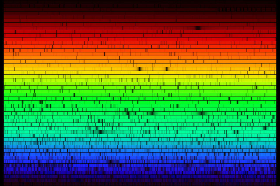 Das Spektrum der Sonne wurde so lang gezogen, dass es in vielen Zeilen übereinander abgebildet wurde. Oben sind rote Spektralfarben, unten blaue und in der Mitte leuchtet das Spektrum gelb und grün. Die vielen dunklen Linien absorbieren Licht bestimmter Elemente oder Moleküle.