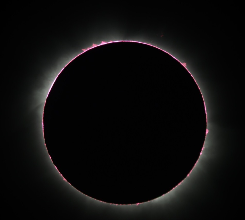 Die dunkle Silhouette des Mondes ist von Protuberanzen und zarten Schleiern der Sonnenkorona umgeben.