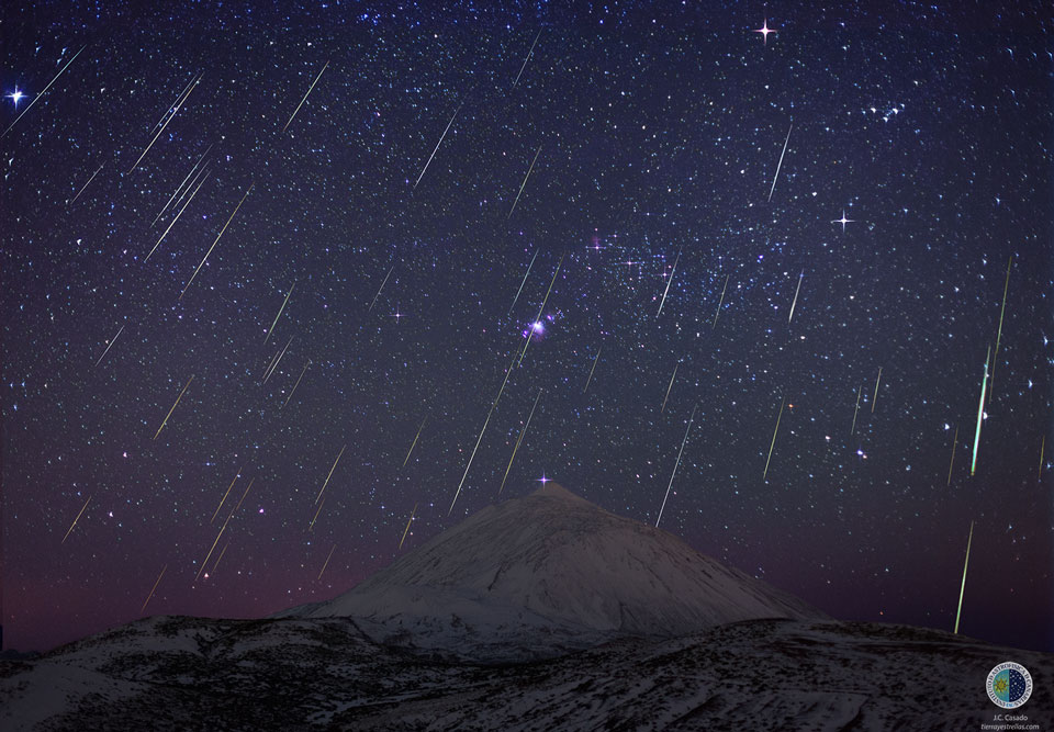 Über dem Vulkan Teide auf Teneriffa leuchtet der helle Stern Rigel. Meteore der Geminiden strömen vom Himmel herab. Dahinter leuchtet das Sternbild Orion.