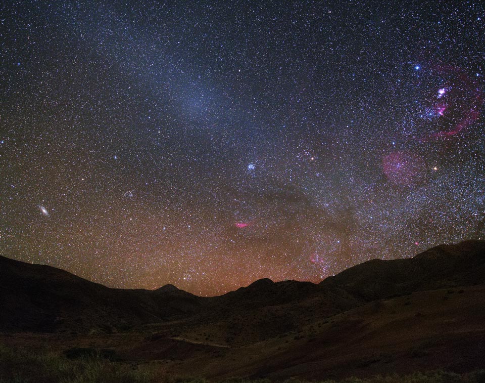 Der Himmel über einer Bergkette ist von zahllosen Sternen, Nebeln und Galaxien bedeckt. In der Mitte leuchtet ein heller Fleck, es ist der Gegenschein.